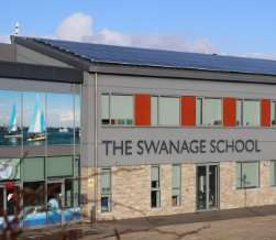 The front of The Swanage School on a clear day, with solar panels along the pitched roof above the main entrance.